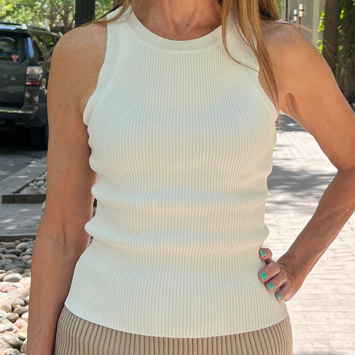 Close up of white crewneck racer back tank with ribbed texture. Model is wearing it with a taupe skirt. She's standing on a sidewalk.