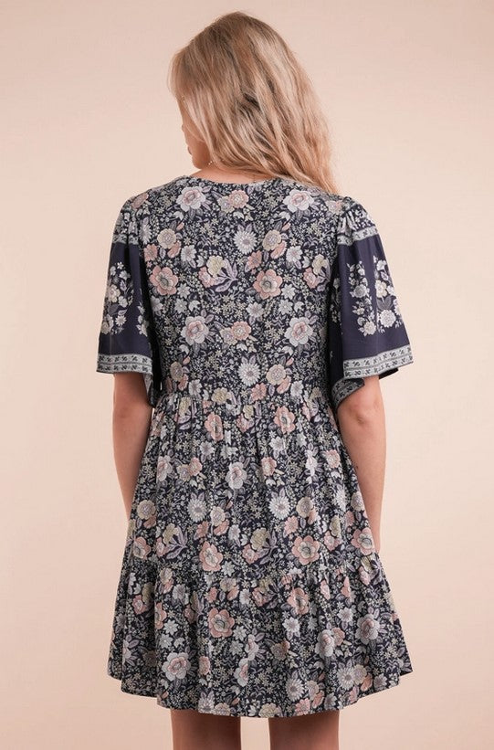 Flowy navy dress has a springy pink and cream floral pattern. The sleeves are slightly loose for a flutter look, and the v-neck bodice is buttoned up the front.