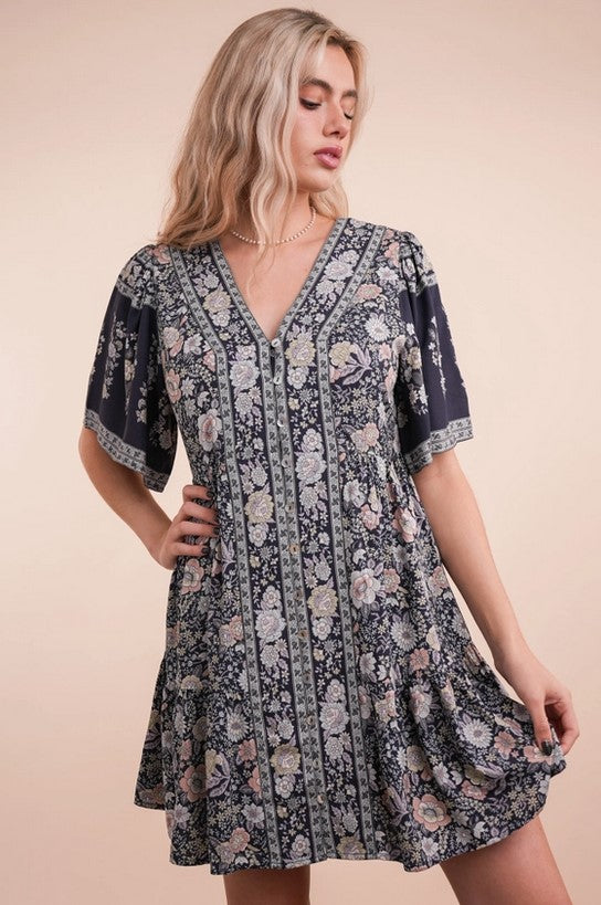 Flowy navy dress has a springy pink and cream floral pattern. The sleeves are slightly loose for a flutter look, and the v-neck bodice is buttoned up the front.