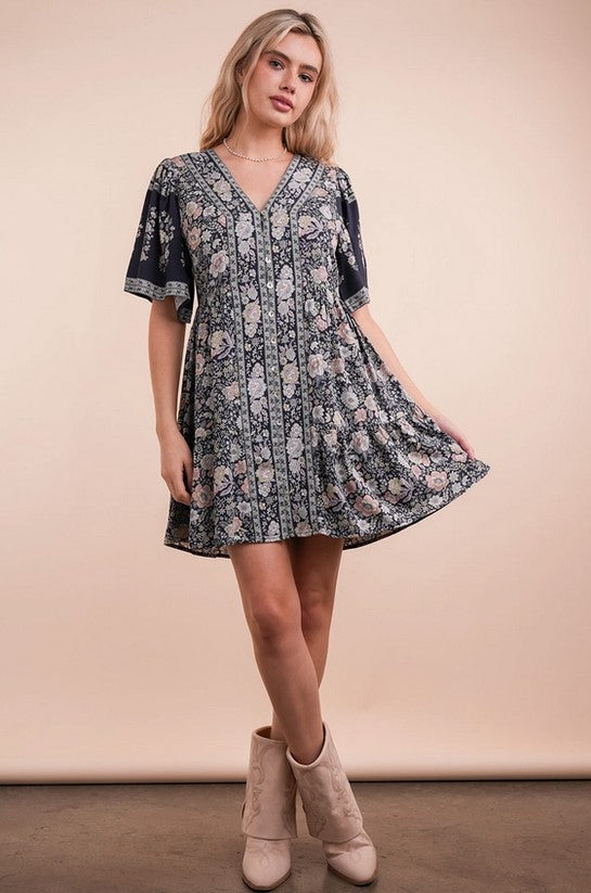Flowy navy dress has a springy pink and cream floral pattern. The sleeves are slightly loose for a flutter look, and the v-neck bodice is buttoned up the front.