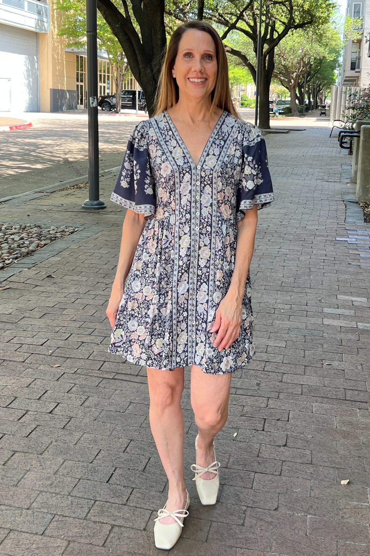 Flowy navy dress has a springy pink and cream floral pattern. The sleeves are slightly loose for a flutter look, and the v-neck bodice is buttoned up the front.