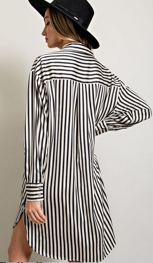 Back view of black and white striped shirt dress made of satin material. Dress has a breast pocket and shirt cuffs.