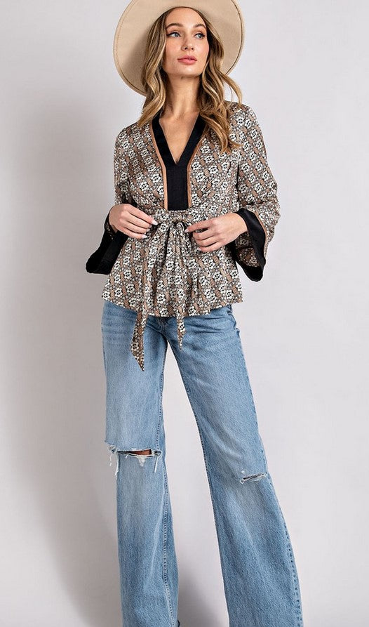 Taupe and black boho-inspired blouse has a tie front and bell sleeves for a boho take on a kimono shape. Model is wearing it with a tan western hat and jeans.