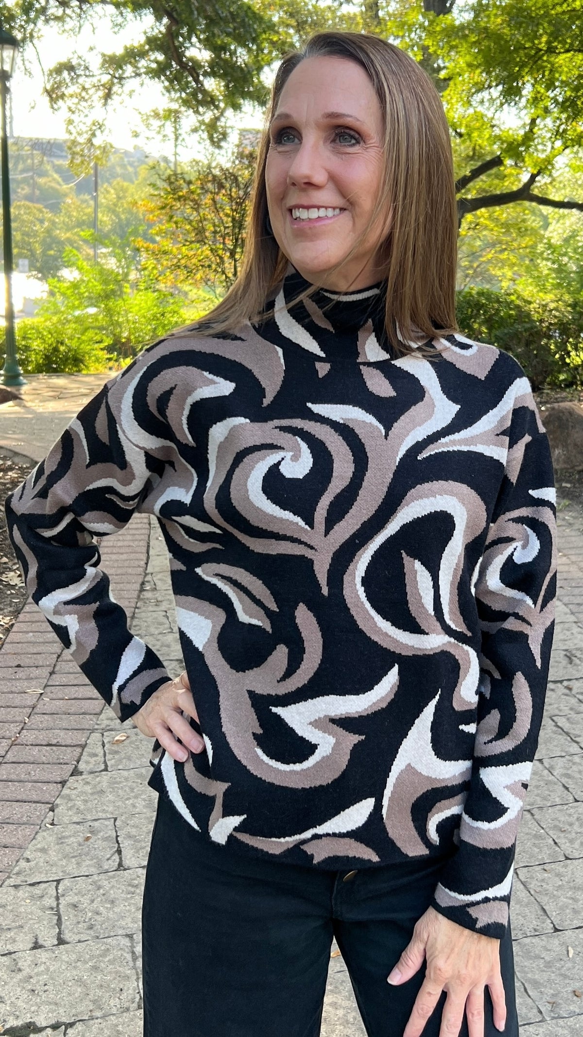 Image is of the front side of the Black and Taupe Abstract Print Sweater on a brunette model who is also wearing jeans.