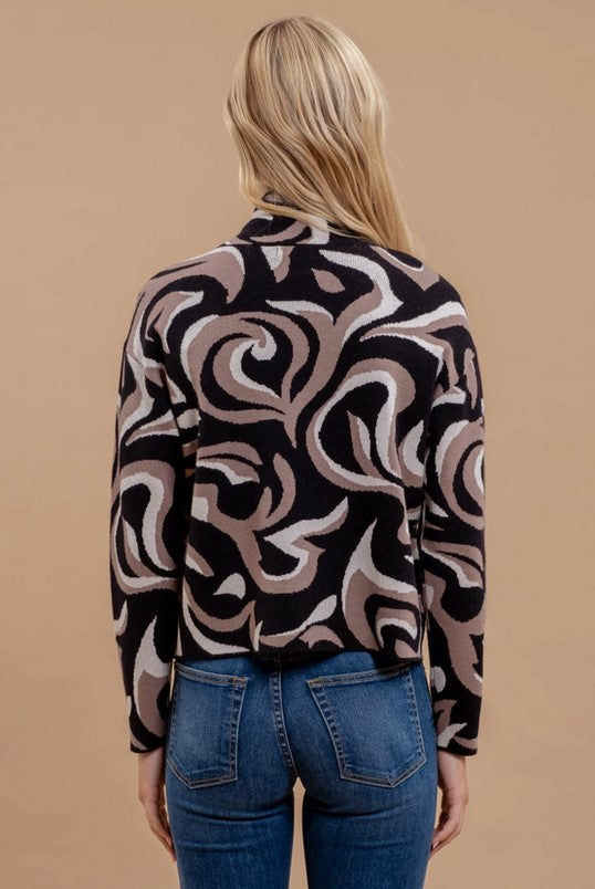 Image is of the back side of the Black and Taupe Abstract Print Sweater on a blonde model who is also wearing jeans.