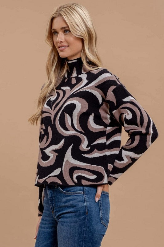 Image is of the Black and Taupe Abstract Print Sweater from the side, worn by a blonde model who is wearing it with jeans.