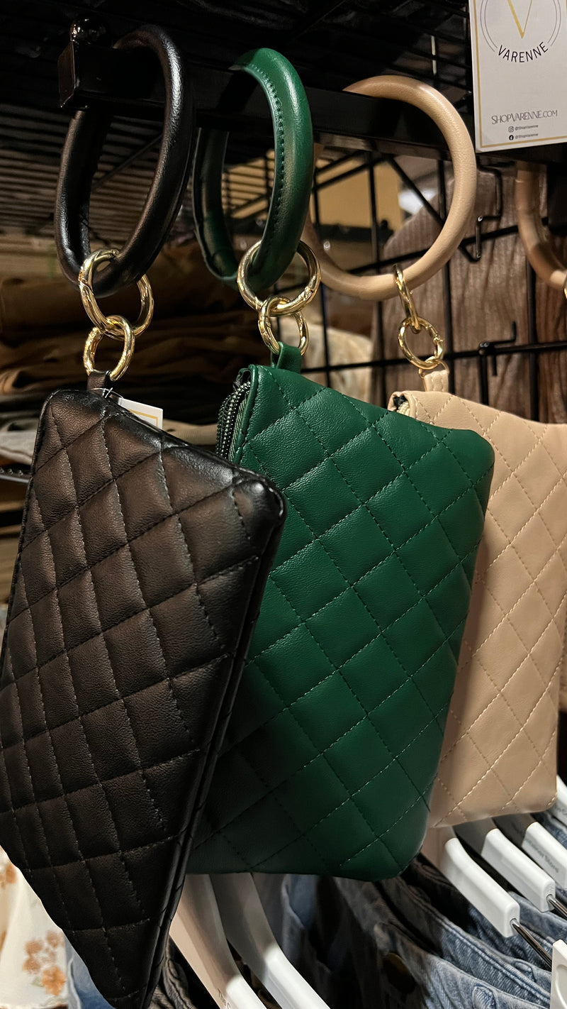 Three quilted wristlets with O-ring wrist straps. The left wristlet is black, the middle is forest green, and the right is khaki. They are hanging on the end of a clothing rack.