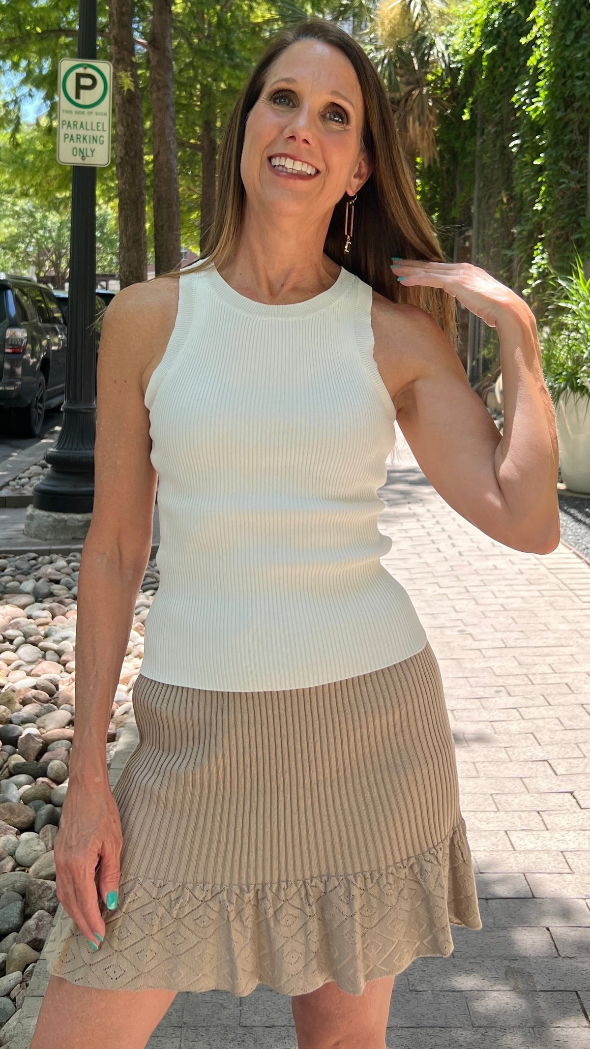 Earrings with a rectangular gold shape with synthetic andalusite stone. Earrings are modeled by a woman wearing a crew neck tank top and taupe ruffle mini skirt. She's standing on a sidewalk. 