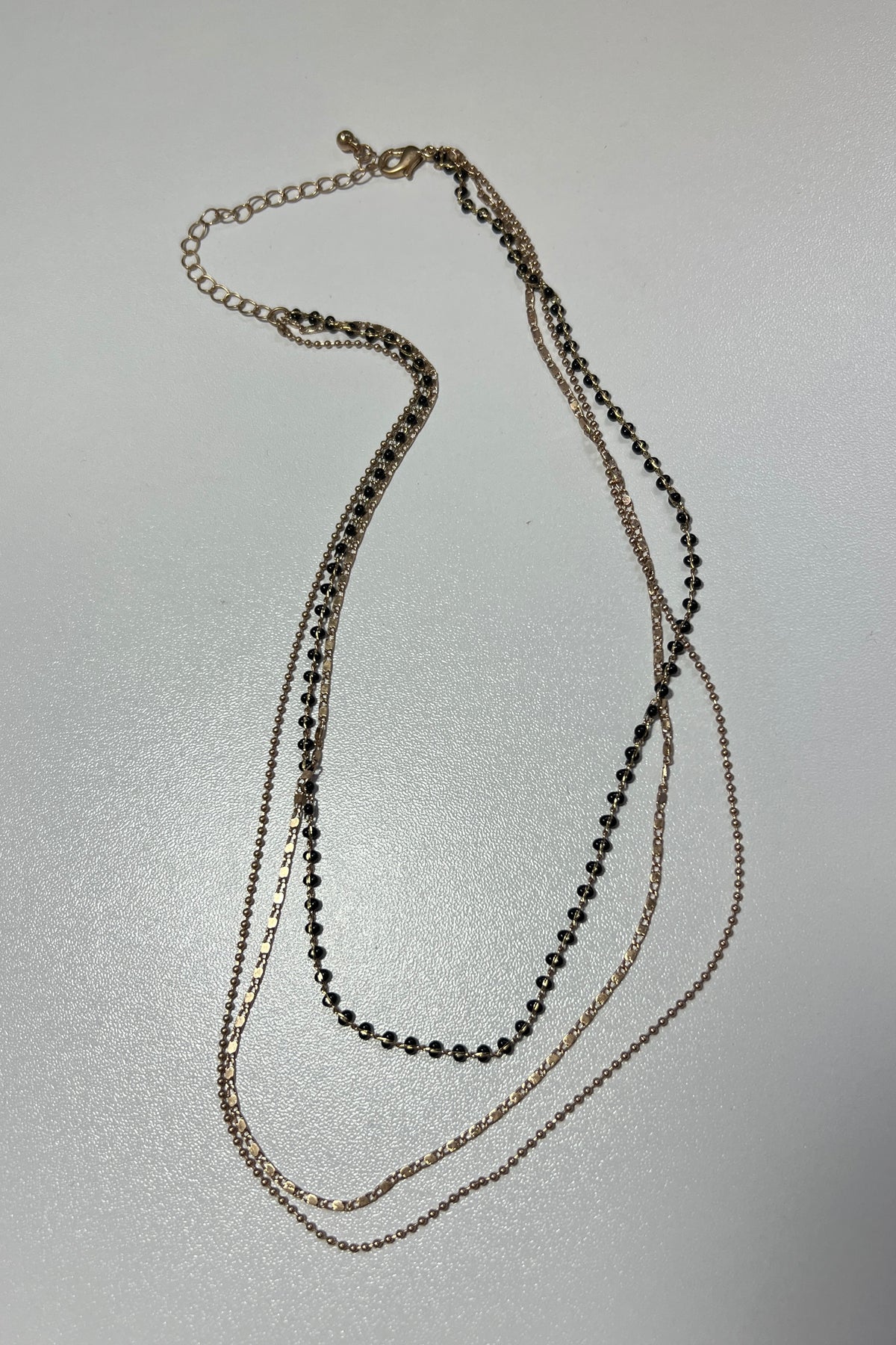 A multi-strand necklace of two gold chains and one black-beaded strand. Pictured on a white background.