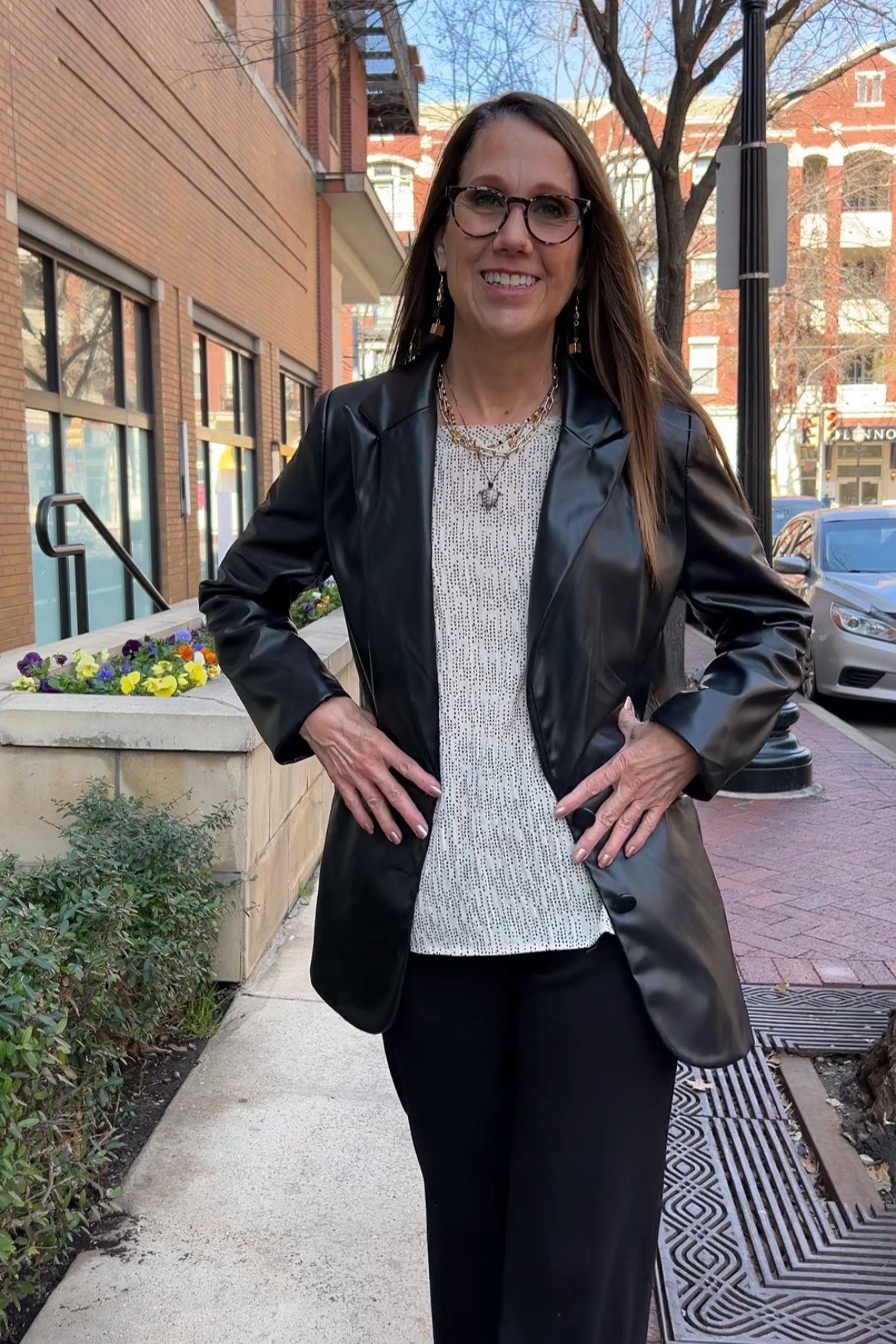 Dolman sleeve ivory-colored blouse with a dainty dot pattern. The top has a boat neckline and smocked cuffs. Model is wearing it with black pants and a black leather blazer. It's styled with chunky necklaces.