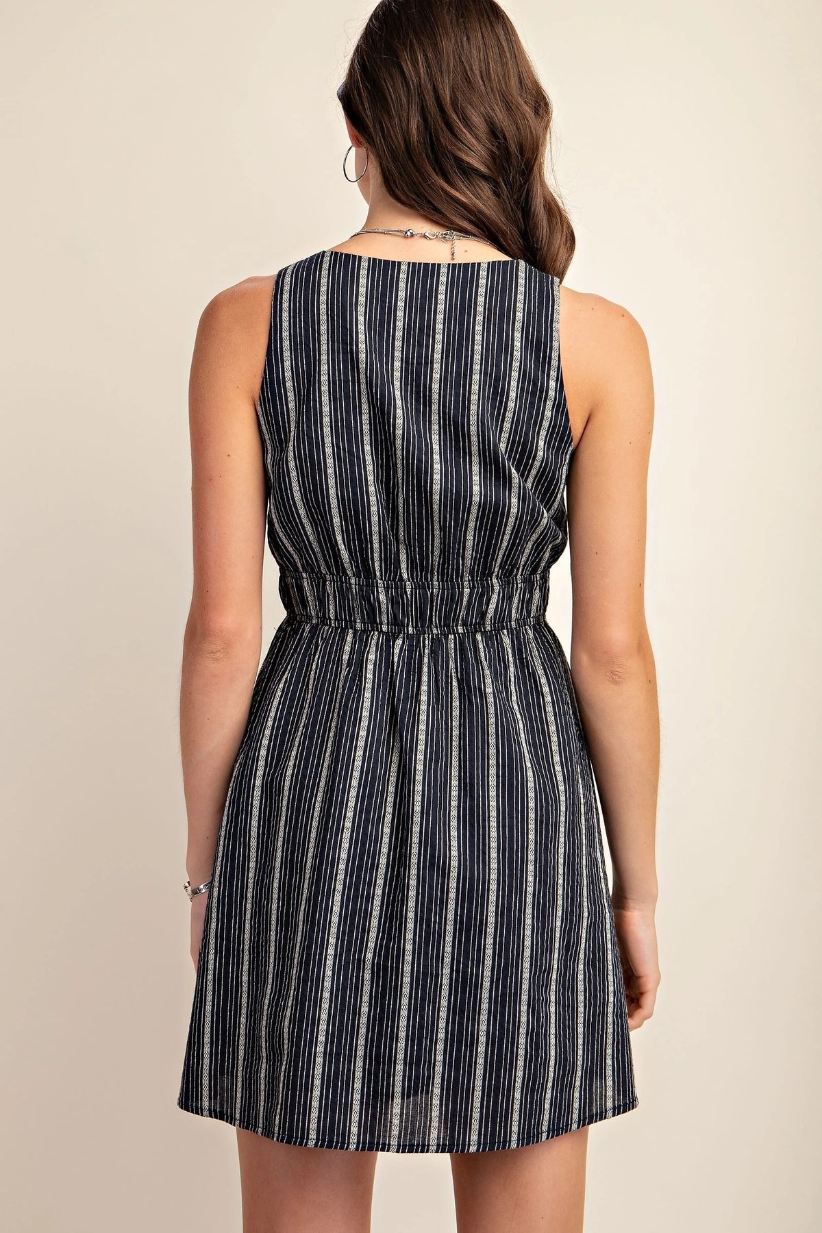 Back side of midnight blue sleeveless dress with beige patterned stripes. It has an elasticized waist and side pockets.