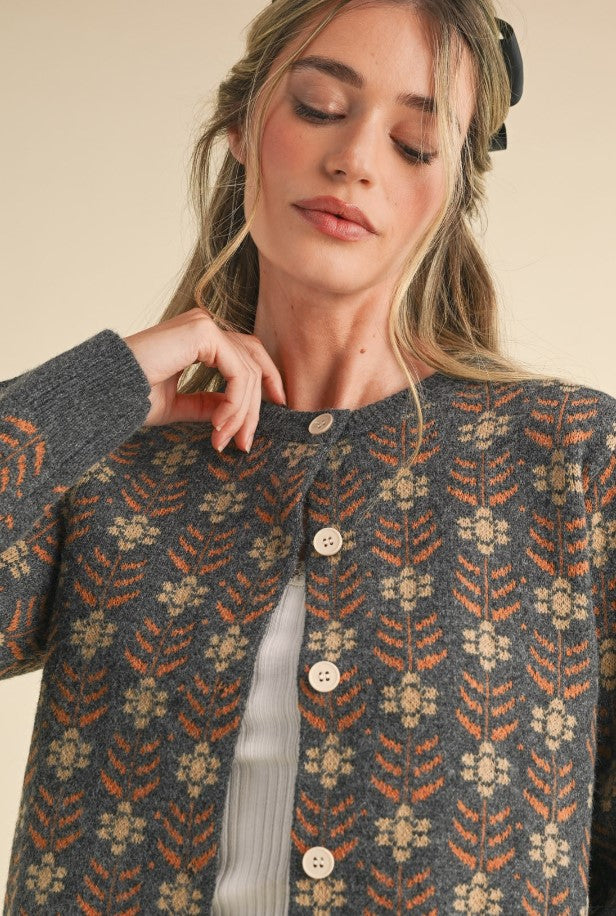 Closeup view of gray cardigan. It's a great winter staple to layer for warmth. It has a rust/cinnamon and ivory floral pattern on a gray background.