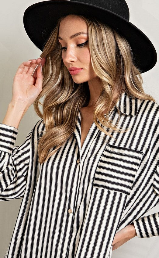 Close up view of black and white striped shirt dress made of satin material. Dress has a breast pocket and shirt cuffs. 