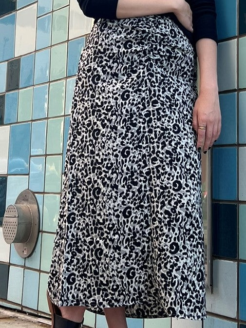 Midi length gray and black leopard print pencil skirt with a side zipper and ruched front. Model is standing in front of a tiled wall.