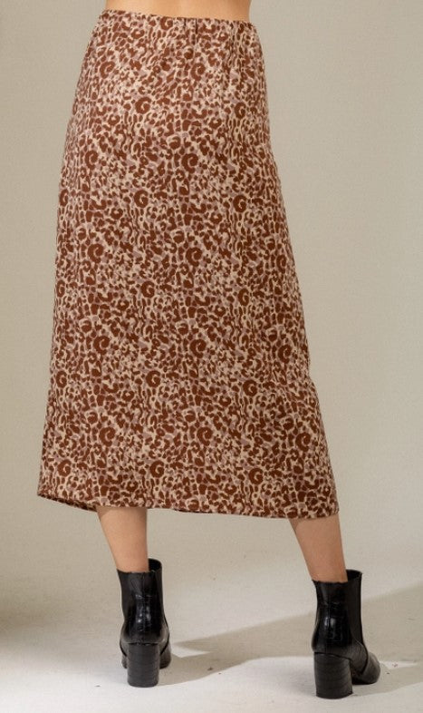 Midi length rust and beige leopard print pencil skirt with a side zipper and ruched front. Model is standing in front of a beige wall and is wearing black booties.