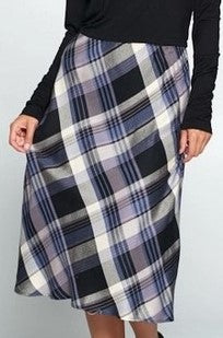 Midi length loose pencil skirt in black, blue, gray, and white tartan style plaid. Model is wearing it with a black shirt and is standing in front of a white wall. 
